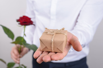 Cropped close up photo portrait of handsome charming happy cheerful positive man holding small little present and bright rose isolated grey background