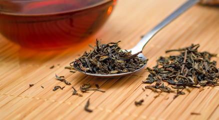 Black leaf tea on a spoon, brewed drink tea in a cup on the table.