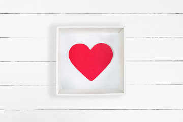 Red paper heart in white cardboard box on white wooden background. Valentine's Day concept