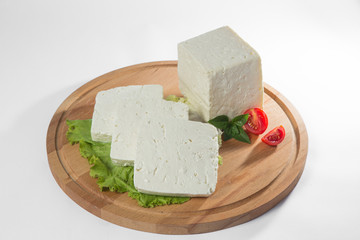 White cheese with some garnitures such as lettuce, cherry tomato slice and basil on a wooden plate, white background
