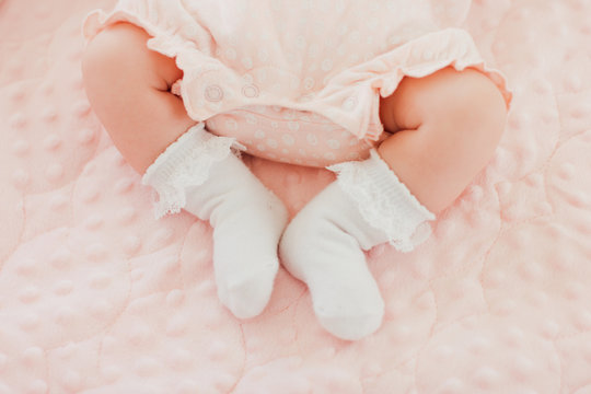 Baby feet in white socks, baby lying on bed, baby's legs, pink background. Newborn, girl