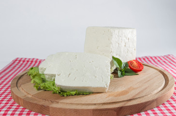White cheese with some garnitures such as lettuce, a slice of cherry tomato and bassil on a wooden plate with houndstooth red and white table sheet