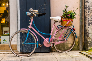Fototapeta na wymiar Pink bicycle with flowers near the wall in the beautiful island of Ortigia in Sicily, Italy
