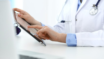 Woman doctor using tablet computer while sitting in hospital office closeup. Healthcare, insurance and medicine concept