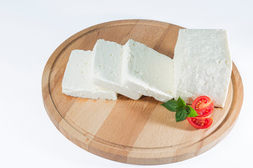 White cheese with some garnitures such as lettuce, cherry tomato slice and basil on a wooden plate, white background