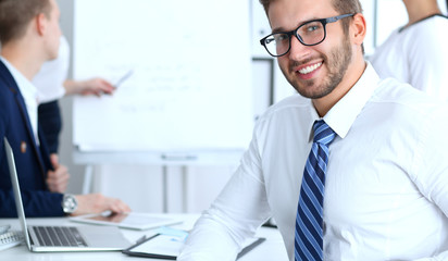 Business people at meeting in office. Focus at cheerful smiling bearded man wearing glasses. Conference, corporate training or brainstorming of people group. Success and negotiation concept