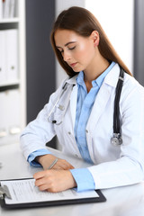 Doctor woman filling up medical form while sitting at the desk in hospital office. Physician at work. Medicine and health care concept