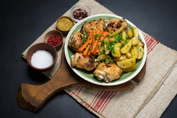 Baked chicken legs with potatoes and carrots under spices and seasonings