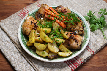 Baked chicken legs with potatoes and carrots under spices and seasonings