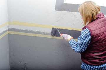 female painting a wall with masking tape and roller