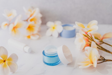 Fototapeta na wymiar group of skincare products including moisturiser scrub and hand cream pots on marble table with exotic frangipani flowers
