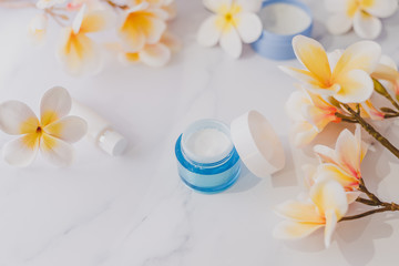 group of skincare products including moisturiser scrub and hand cream pots on marble table with exotic frangipani flowers