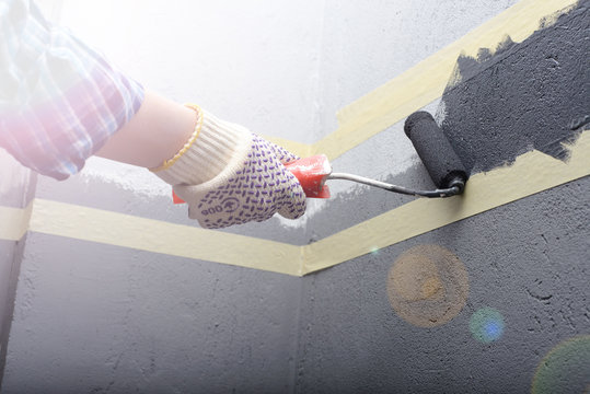 female painting a wall with masking tape and roller