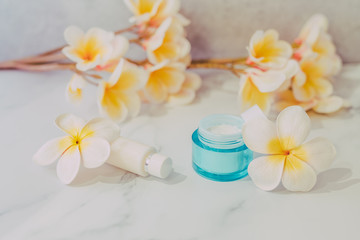 group of skincare products including moisturiser and hand cream pots on marble table with exotic frangipani flowers