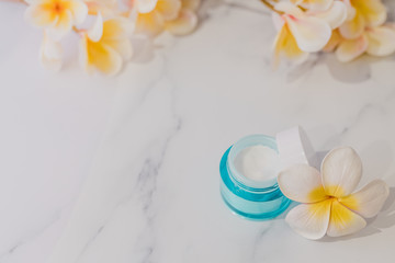 skincare moisturiser product on marble table with exotic frangipani flowers