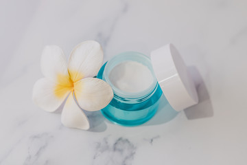 skincare moisturiser product on marble table with exotic frangipani flowers