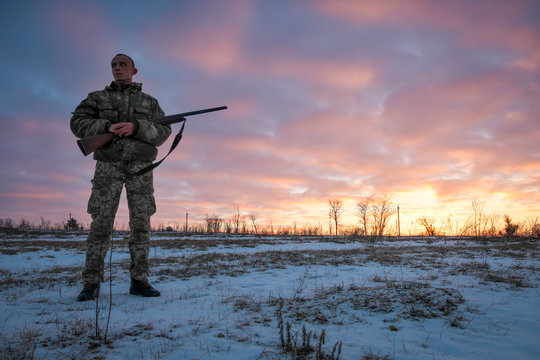Winter hunting at sunrise. Hunter moving With Shotgun and Looking For Prey.