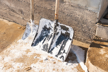 Wide snow shovel against the brick wall on a snowy yard. Severe weather conditions in winter