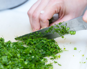Female hands chopping the dill leaves on a cutting board with a knife. The concept of cooking