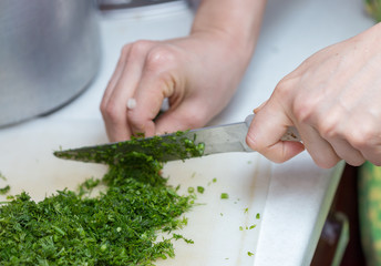 Female hands chopping the dill leaves on a cutting board with a knife. The concept of cooking