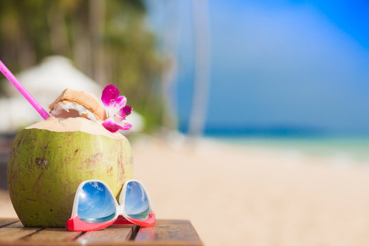 Fresh coconut cocktail decorated with orchid flower and sunglasses on a tropical beach