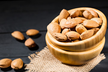 Almonds with shell in wooden bowls on slate background