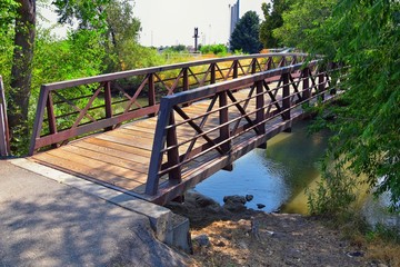 Views of Jordan River Trail Pedestrian and Train Track Bridge with surrounding trees, Russian Olive, cottonwood and muddy stream along the Wasatch Front Rocky Mountains, in Salt Lake City, Utah.