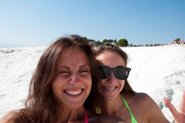 Fototapeta premium Funny selfie with sister. Happy frineds girls with suntan. Natural travertine in Pamukkale. Beach. Cotton castle in Turkey. Summer vacation. Selfie. Dead sea salty shore. Sexy girl. Friendship