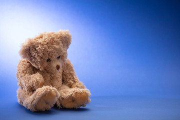 Teddy bear sad, holding his head, sitting in blue empty room background, copy space