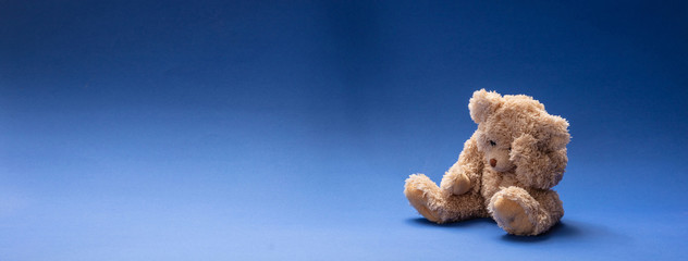 Teddy bear sad, holding his head, sitting in blue empty room background, banner
