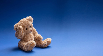 Teddy bear sad, holding his head, sitting in blue empty room background, copy space