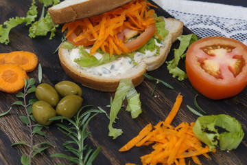 Healthy vegetarian sandwich with carrot, Tomato, lettuce and spices, served on an wooden board.