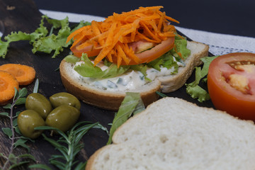 Healthy vegetarian sandwich with carrot, Tomato, lettuce and spices, served on an wooden board.
