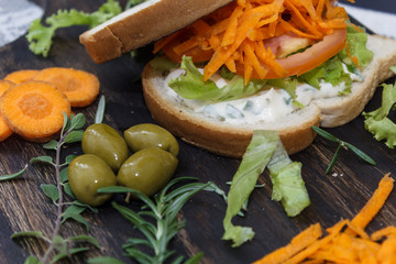 Obraz na płótnie Canvas Healthy vegetarian sandwich with carrot, Tomato, lettuce and spices, served on an wooden board.