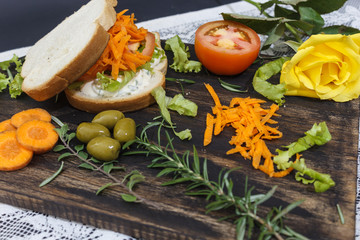 Obraz na płótnie Canvas Healthy vegetarian sandwich with carrot, Tomato, lettuce and spices, served on a wooden board, with an yellow rose.