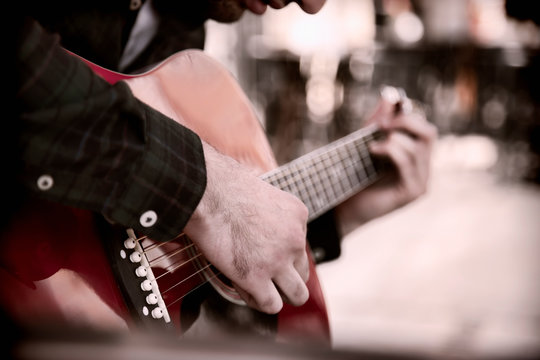A Busker singing and playing guitar on the streets of old European city. Caucasian man playing the guitar outdoors.Selective focus on hand.