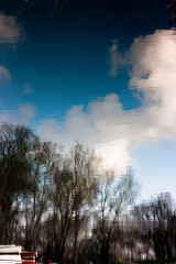 Blurry nature, reflection of boats, woods, blue sky and clouds in river water