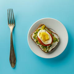 Healthy avocado, egg open sandwiches on a plate with cherry tomatoes on blue background