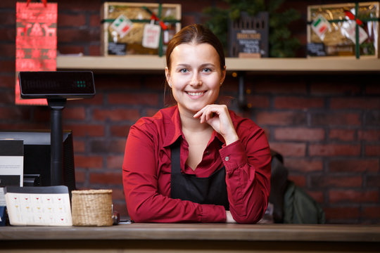 Photo of woman seller in black apron standing behind cashier