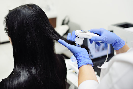 doctor dermatologist diagnoses the structure of the hair of a young pretty girl with a special tool - a trichoscope. Trichology, trichogram