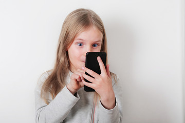 Portrait of a smiling little blonde girl looking at mobile phone , smartphone on white background