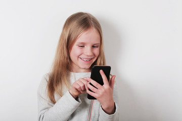 Portrait of a smiling little blonde girl looking at mobile phone , smartphone on white background