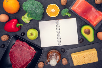 Photo of food products for diet, clean notepad on black stone table.