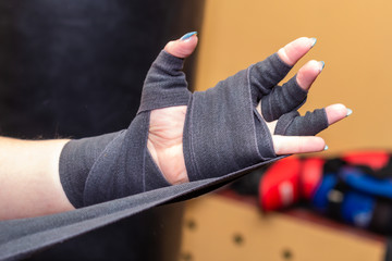 Woman is wrapping hands with grey boxing wraps. Closeup