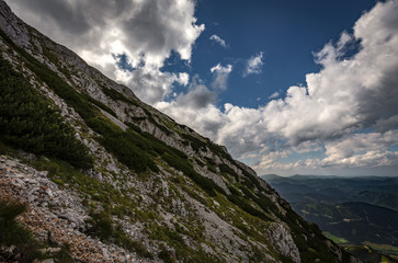 Scenic view on rocky route Nandsteig from Puchberg to Kaiserstein on Rax plateau, Schneeberg masif with dramatic cloudy sky and pine trees, Raxalpe, Lower Austria