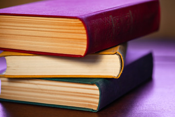 close-up old big books with red, yellow and green covers are lying on a wooden table in a purple light