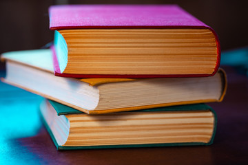 close-up old big books with red, yellow and green covers are lying on a wooden table in blue light