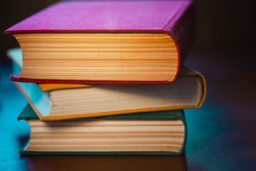 close-up old big books with red, yellow and green covers are lying on a wooden table in blue light