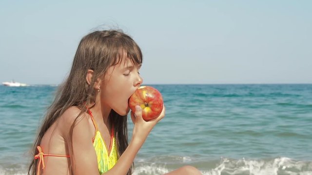 Child having snack on the beach. Little girl eats an apple on the beach against the background of the sea.