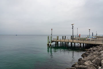 Outdoor scenery of riverside, embankment and pier at Geneva Lake without people with background of overcast cloudy sky in Lausanne, Switzerland.